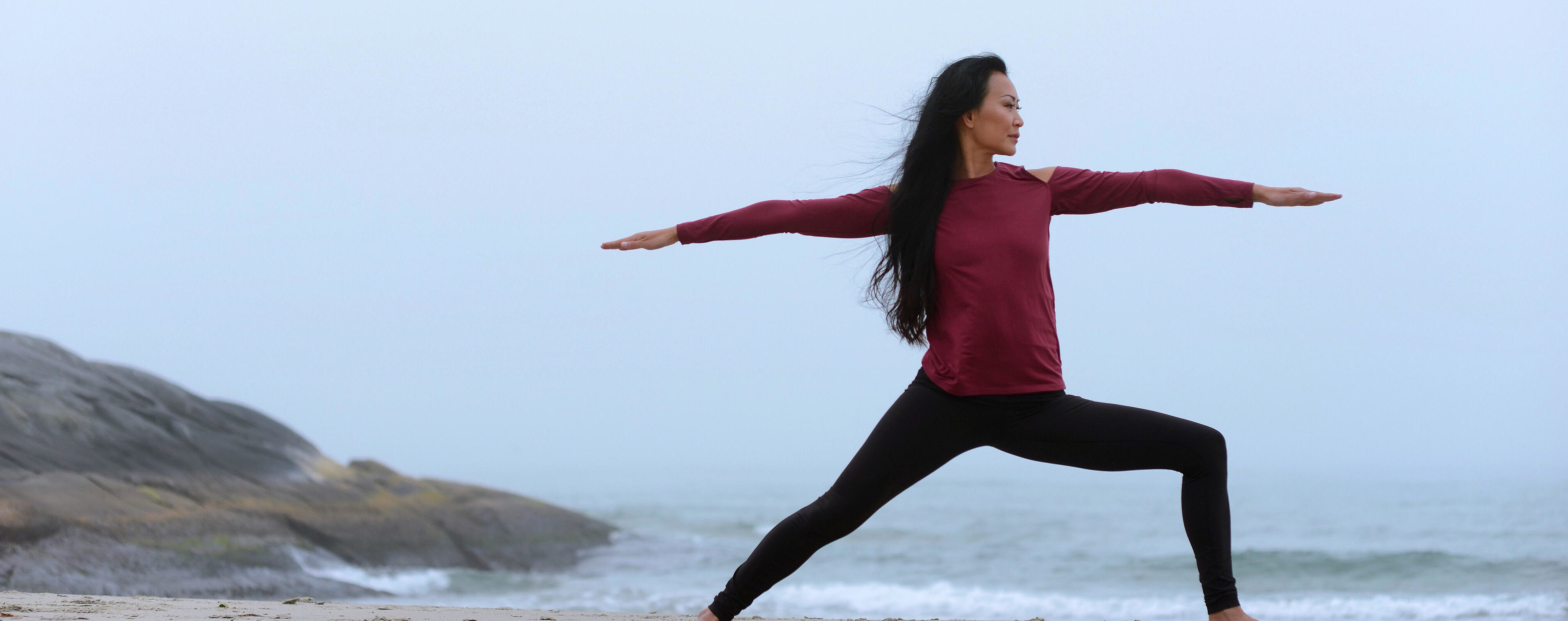Yogainstruktør i kriger to-posisjon på stranden ved sjøen